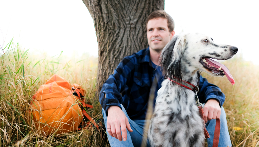Oranži seljakotiga mees istub murul puu all ja tema ees istub koer