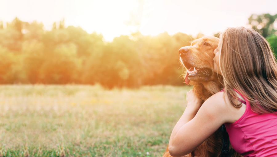 Naine istub oma koeraga põllul ja suudleb koera nägu